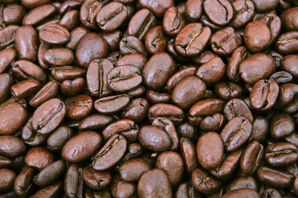 An image showcasing the rich Sumatra Coffee Beans; capture the dark, earthy hues of the beans, glistening with oils, as they rest on a rustic wooden surface, surrounded by hints of aromatic steam